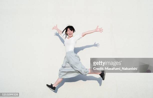photo of asian woman jumping with smile in front of white wall - japanese woman stock pictures, royalty-free photos & images