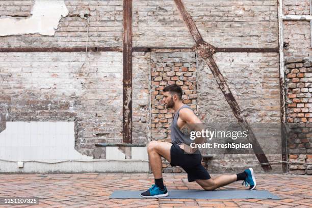 riscaldamento: un uomo muscoloso in abbigliamento sportivo che fa un esercizio affondo basso per prepararsi all'allenamento - affondo foto e immagini stock