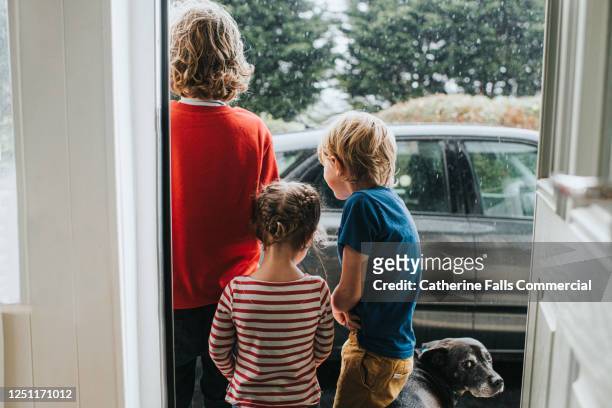 three kids and a dog standing outside front door looking at heavy rain - family in rain stockfoto's en -beelden