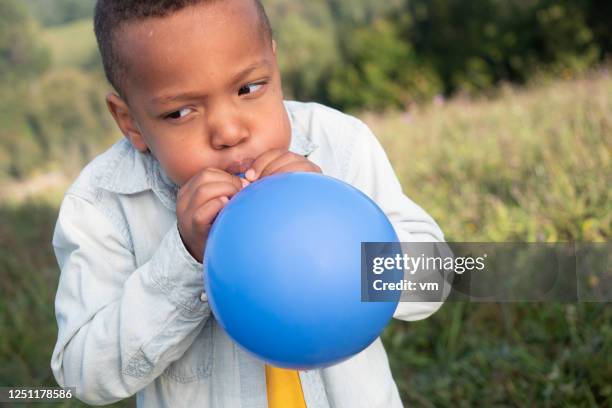 menino de ascendência africana inflando um balão azul - inflating - fotografias e filmes do acervo