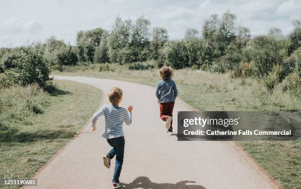 two boys running down a yellow path in bright sun - running in the sun stock-fotos und bilder