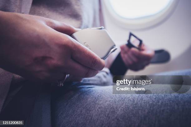 female passenger fastening seat belt while sitting on the airplane for safe flight. - metallic belt stock pictures, royalty-free photos & images