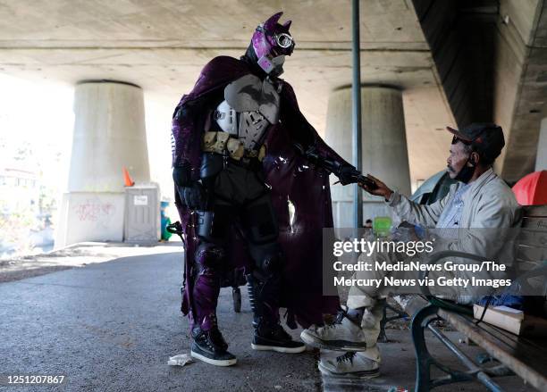Batman, a 19-year-old San Jose man who wants to remain anonymous, hands socks to a homeless man in an encampment under Highway 87 in downtown San...