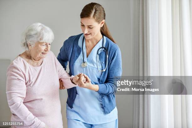 nurse assisting elderly female in walking at home - care stock-fotos und bilder