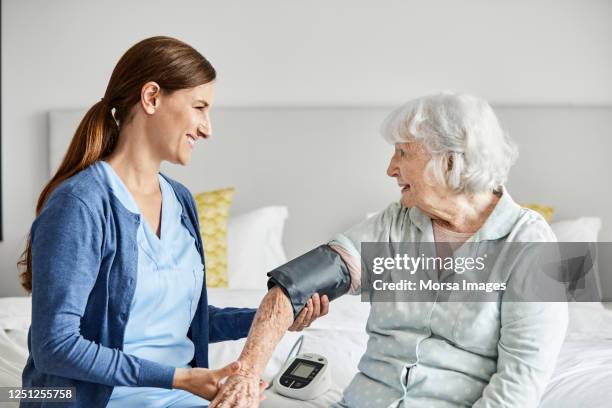 caregiver examining blood pressure of senior woman - hypertension stock-fotos und bilder