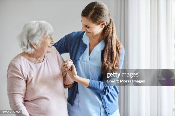 smiling nurse assisting senior female in walking - nurse helping old woman at home stockfoto's en -beelden