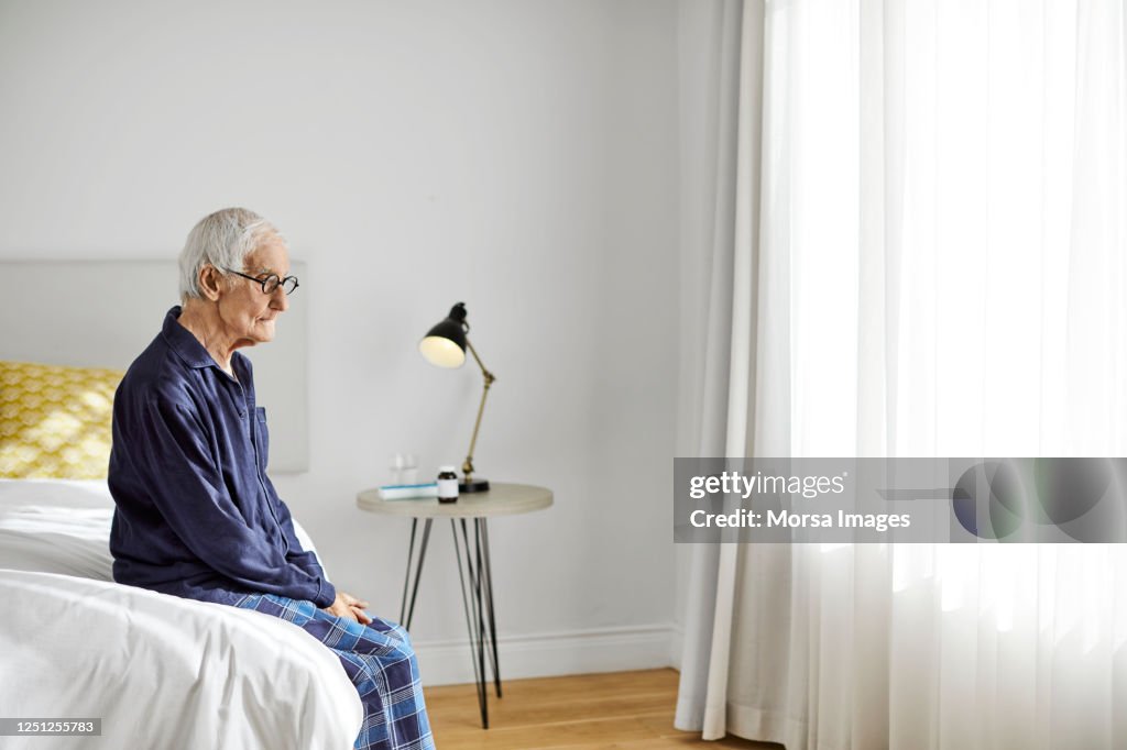 Contemplated senior male sitting on bed