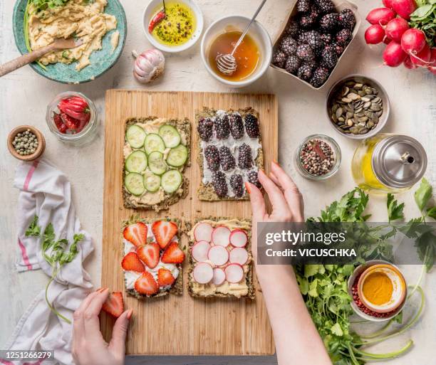 women hands making sandwiches with green healthy gluten free chips bread oder falafel bread with fresh herbs, chickpeas hummus , nuts and olive oil , berries and vegetables on white kitchen table with ingredients. - healthy snacks stockfoto's en -beelden