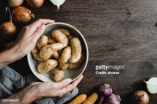 frau hält eine schüssel voller frischer kartoffeln - kitchen table stock-fotos und bilder