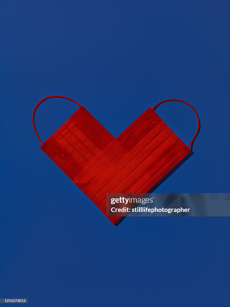 Two red medical face masks shaped as a heart isolated on blue background