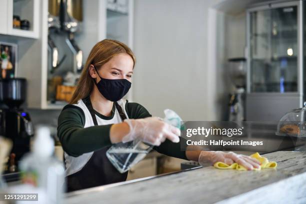 young woman barista with face mask and gloves standing in coffee shop, disinfecting counter. - cloth mask 個照片及圖片檔