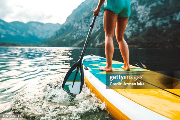 woman in early 30s paddleboarding on lake bohinj in slovenia - paddleboard stock pictures, royalty-free photos & images