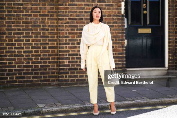 Tiffany Hsu wears a scarf, a white flowing top, pale yellow cropped pants, white heels shoes, a leather crocodile pattern bag, during London Fashion...