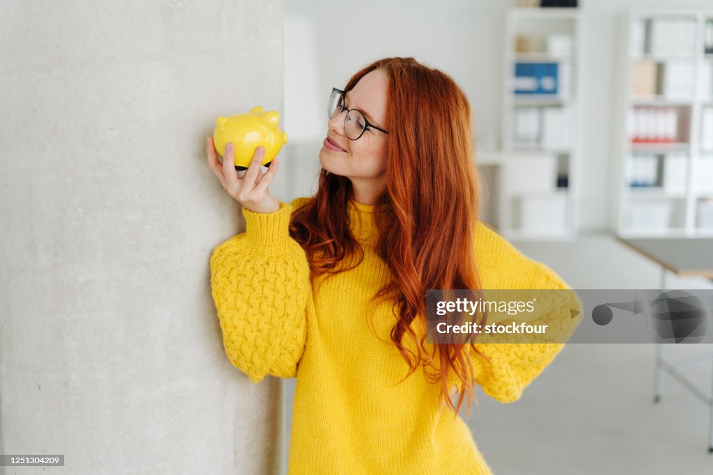 Smiling young woman contemplating a piggy bank