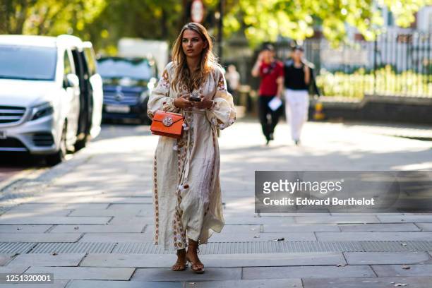 Guest wears a white long dress with brown pixel geometric patterns, an orange leather bag, sandals, during London Fashion Week September 2019 on...