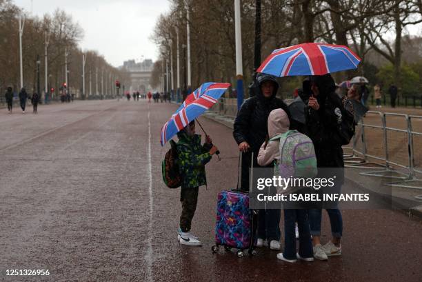 Tourists shelter from the rain beneath Union flag-themed umbrellas on The Mall, near Buckingham Palace in central London on April 10 as preparations...