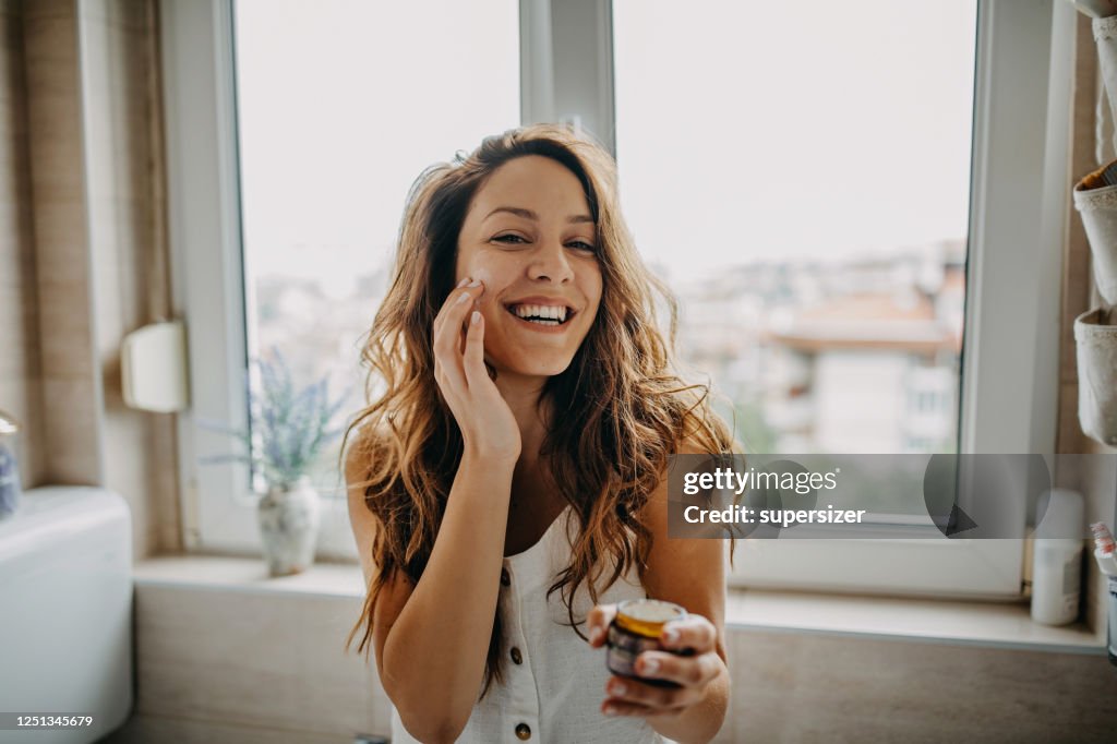 若い女性はフェイシャルクリームを適用します