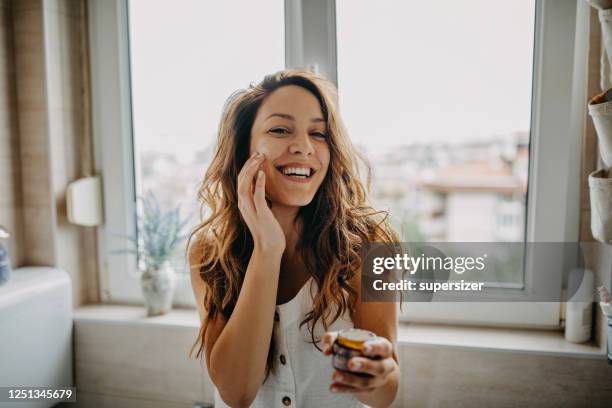 young woman applies facial cream - skin treatment stock pictures, royalty-free photos & images