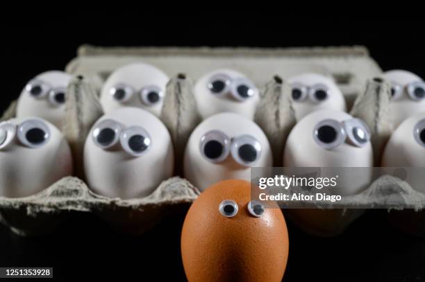 face made with a brown egg in the foreground, in the background many white ar looking to it. - racismo imagens e fotografias de stock