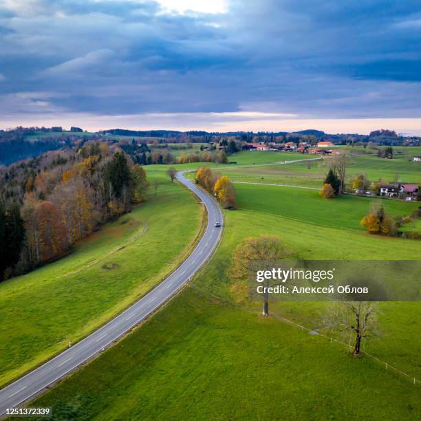 aerial view autumn landscape in bavaria near miesbach. road going into the distance and the peaks of the alps on the horizon. clouds sky, yellow trees and green field - miesbach fotografías e imágenes de stock