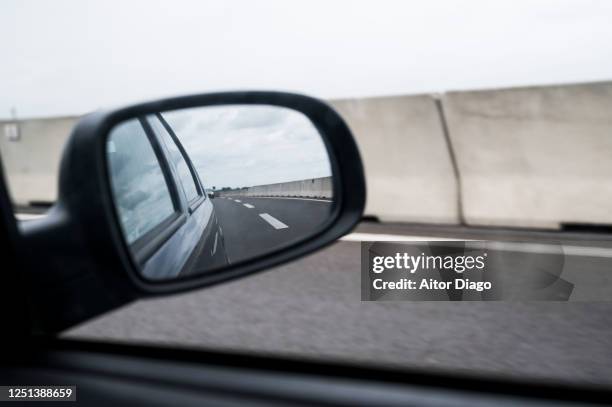 view of the road through the window of a car and its rearview mirror while driving on the road in a cloudy day. germany. - side view mirror foto e immagini stock