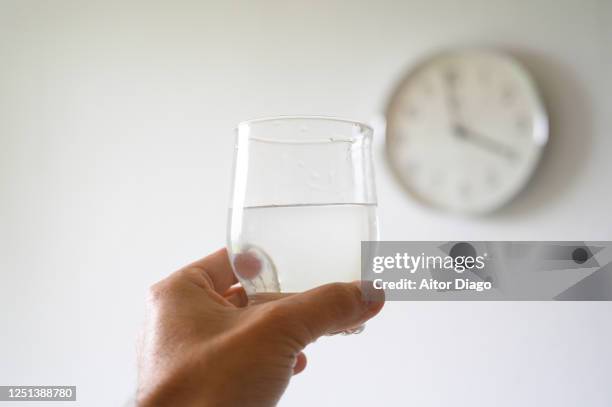 man's hand holding a glass of water, in the background is a wall clock. - glass of water hand ストックフォトと画像