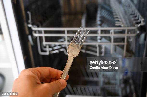 man's hand inserting a fork in the dishwasher. - pastille pour lave vaisselle photos et images de collection