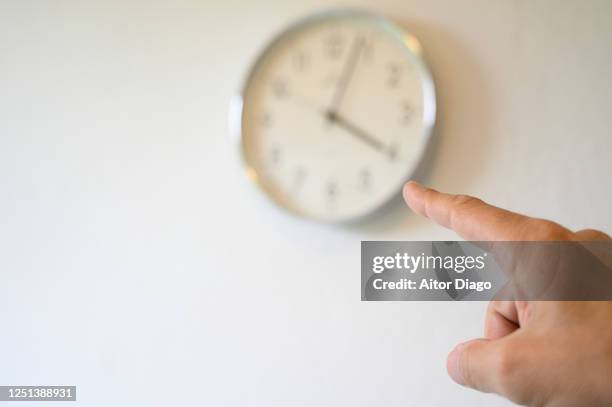 index finger of a man pointing the time on a wall clock. it's 4 o'clock - office hour stock pictures, royalty-free photos & images