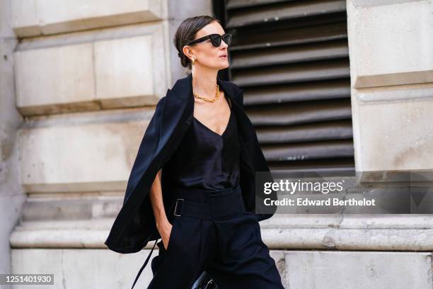 Guest wears sunglasses, a black jacket, a black low neck top, a golden necklace, earrings, during London Fashion Week September 2019 on September 15,...