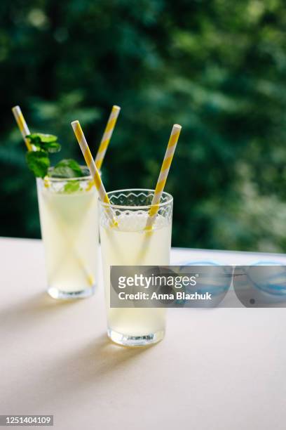 summer cold drink in glass, lemonade on table in sunny day, green trees blurred background - traditional lemonade stock pictures, royalty-free photos & images