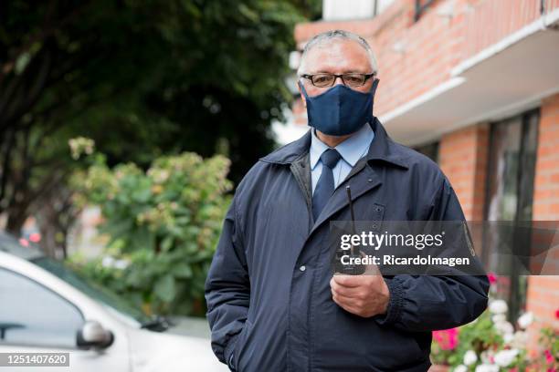 de portier van het gebouw bekijkt de camera in een portret terwijl het dragen van zijn masker om covid 19 te vermijden - uitsmijter stockfoto's en -beelden