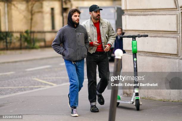 Guest wears a black hooded sweatshirt, a fluffy grey teddy jacket, blue jeans, navy-blue sneakers ; A guest wears a black cap, a light grey lustrous...