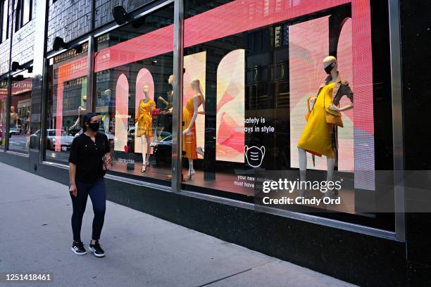 Person wearing a protective mask walks by a Bloomingdale's window display featuring a mannequin wearing a mask as the city moves into Phase 2 of...