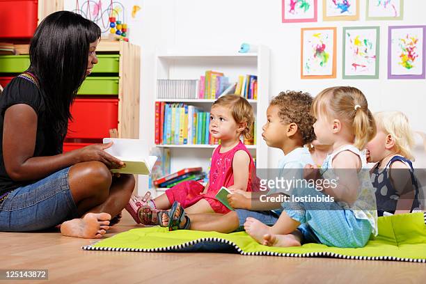 teacher/carer/ childminder reading to a group of toddlers at nursery - nanny stock pictures, royalty-free photos & images