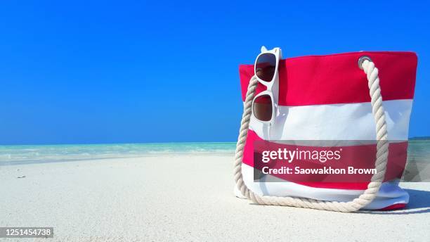 copy space of travel theme with a stripped summer bag and sunglasses standing on sandy exotic beach with sea and sky background - beach bag foto e immagini stock