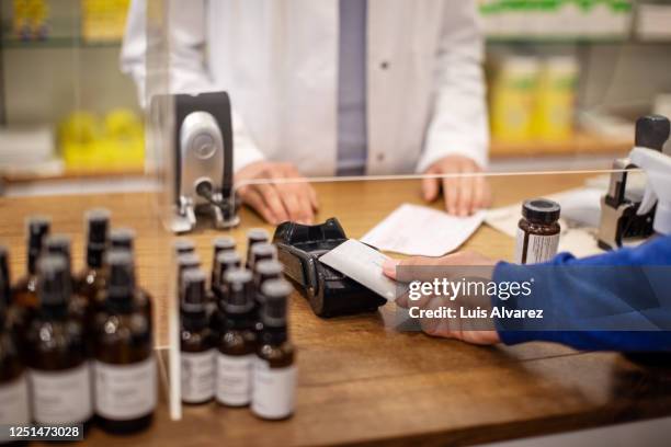 customer making contactless payment at pharmacy - homeopatía fotografías e imágenes de stock