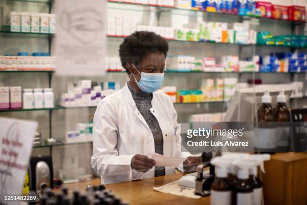 woman pharmacist with face mask working in a drug store - pharmacy mask stock pictures, royalty-free photos & images