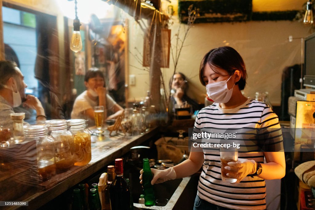 Bar owner serving beer with protective plastic glove from behind protective plastic curtain