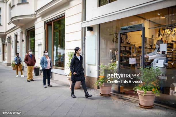 people waiting in the queue outside pharmacy with social distancing - retail place stock pictures, royalty-free photos & images