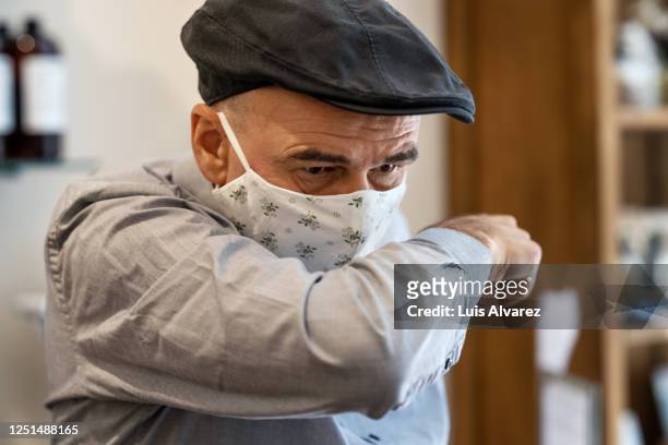 senior man covering mouth with elbow while sneezing - infectious disease fotografías e imágenes de stock