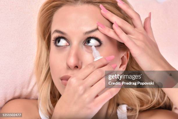 young woman putting eye drops while laying on bed - augentropfen stock-fotos und bilder