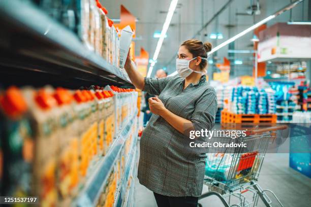 young pregnant woman wearing disposable medical face mask choosing fresh salad in supermarket during coronavirus outbreak. stock photo - juice box stock pictures, royalty-free photos & images