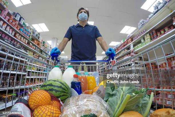 man with face mask and gloves pushing supermarket trolley full of goods. - chariot photos et images de collection