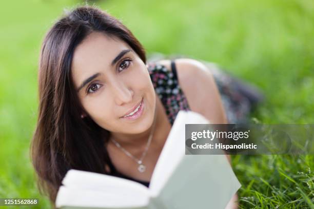 mooie vrouw die op gras ligt dat een boek houdt dat camera glimlacht - woman smiling facing down stockfoto's en -beelden