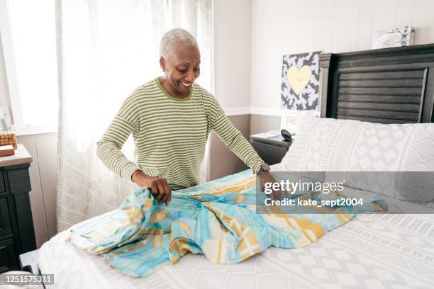 vrolijke hogere vrouw die een deken in haar slaapkamer vouwt - declutter stockfoto's en -beelden