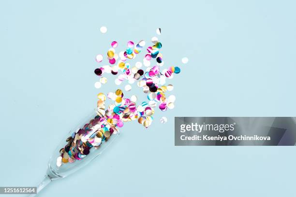 round paper confetti and party streamers poured out of champagne glass on trendy blue background. flat lay style. celebration concept. color of the year 2020 concept. copy space. - serpentina - fotografias e filmes do acervo