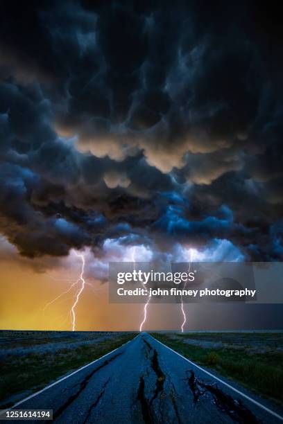 triple lightning bolts with a broken road vanishing into the distance - mammatus cloud stock pictures, royalty-free photos & images