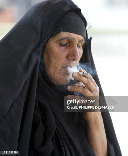 An Iraqi woman in traditional dress smokes a cigarette in the southern city of Basra 08 May 2003. Iraqi health officials were to meet with the UN's...