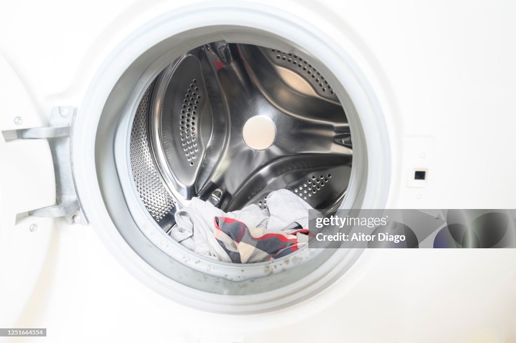 Open washing machine with some laundry inside.