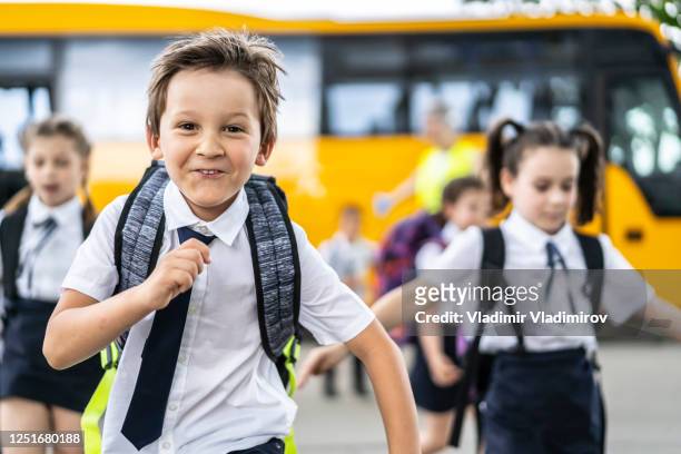 retrato de niño de la escuela, corriendo con sus compañeros de clase después de llegar al autobús escolar, mirando a la cámara. - uniforme fotografías e imágenes de stock